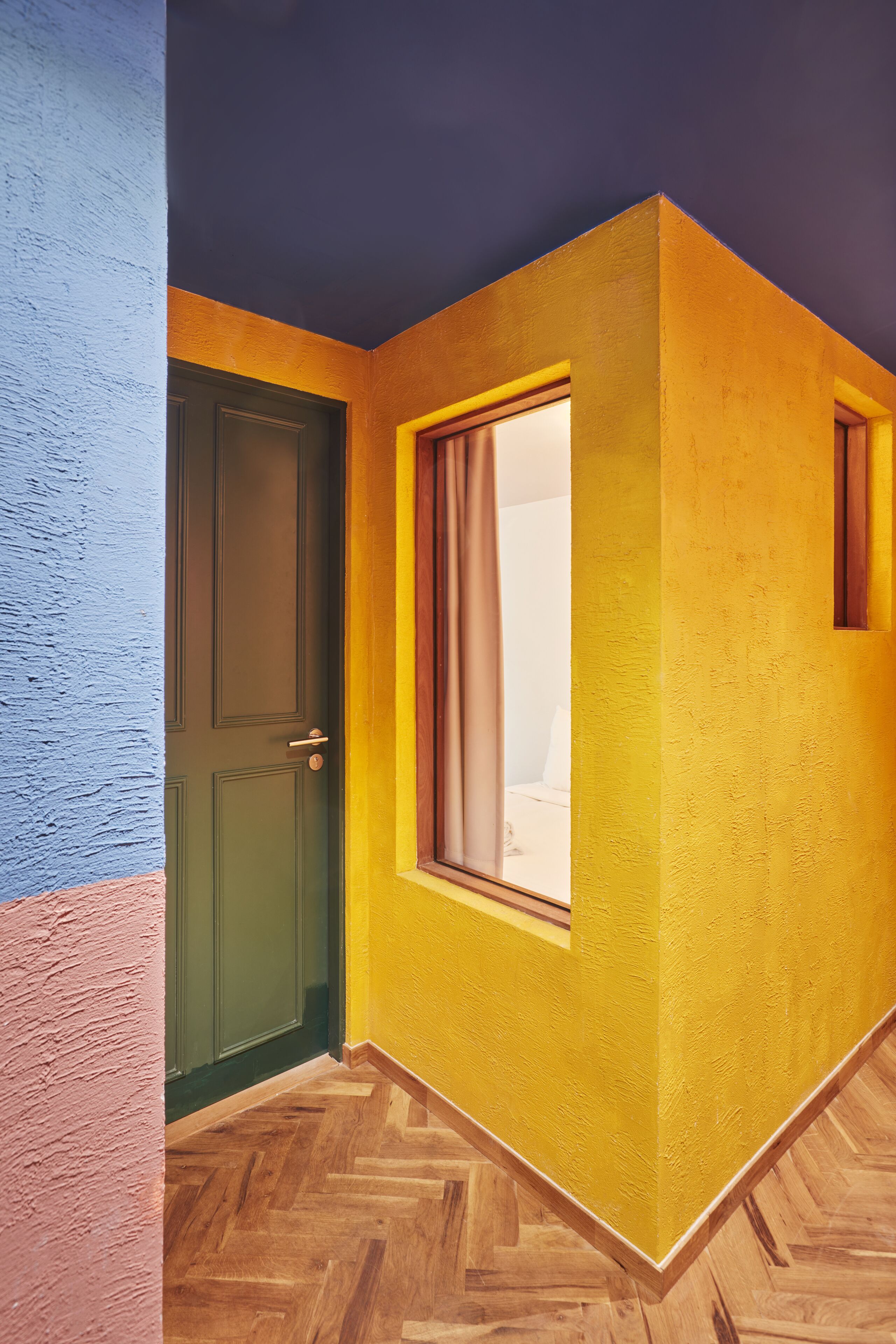Un pasillo con una puerta verde, una ventana con cortinas y una pared amarilla.