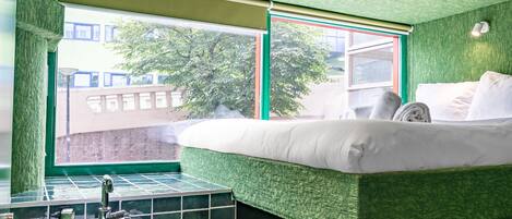Una habitación con cama, ventana, lavamanos y pared verde con textura.