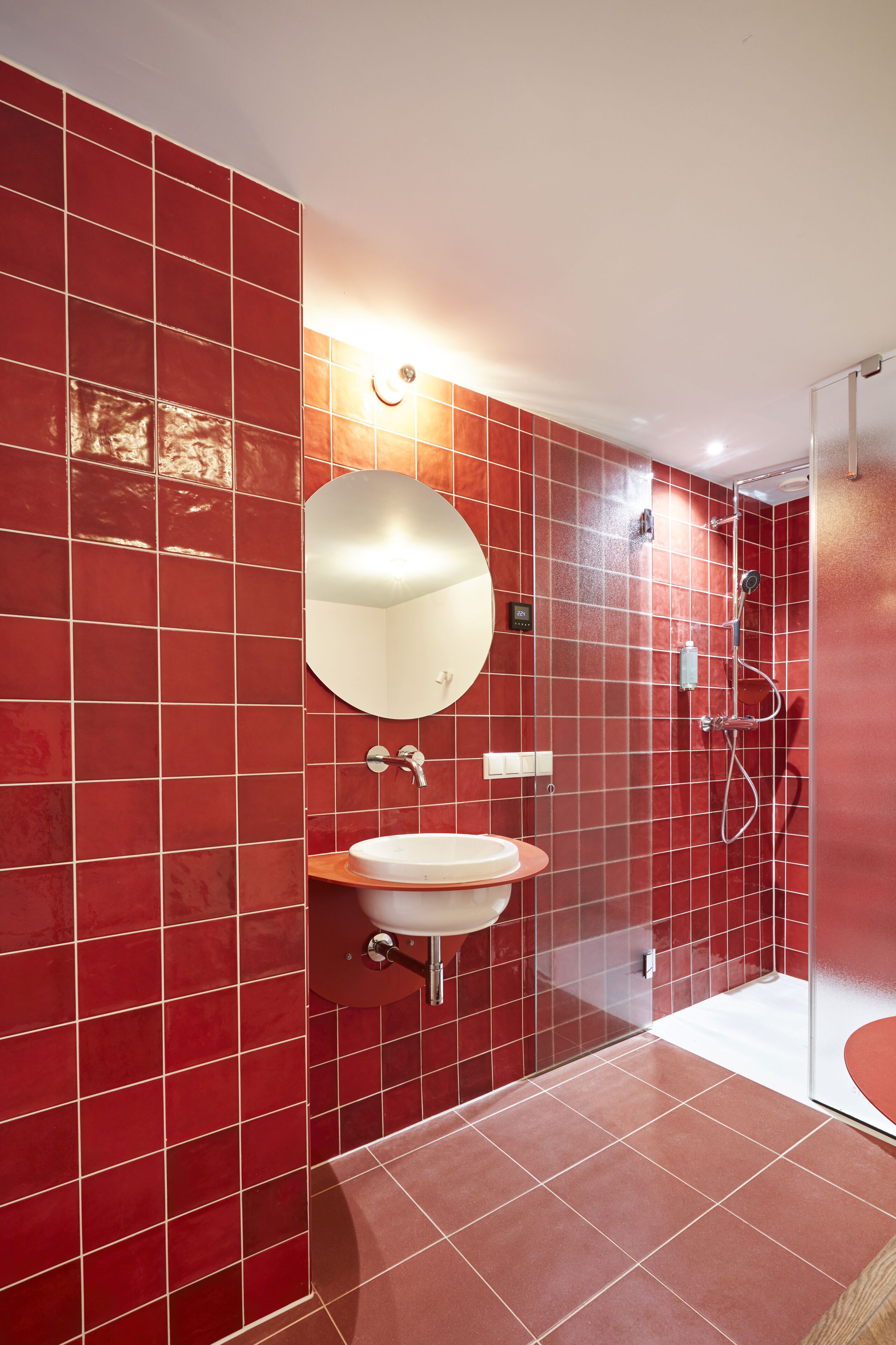 A bathroom with red tiles, a round mirror, a sink, and a shower.