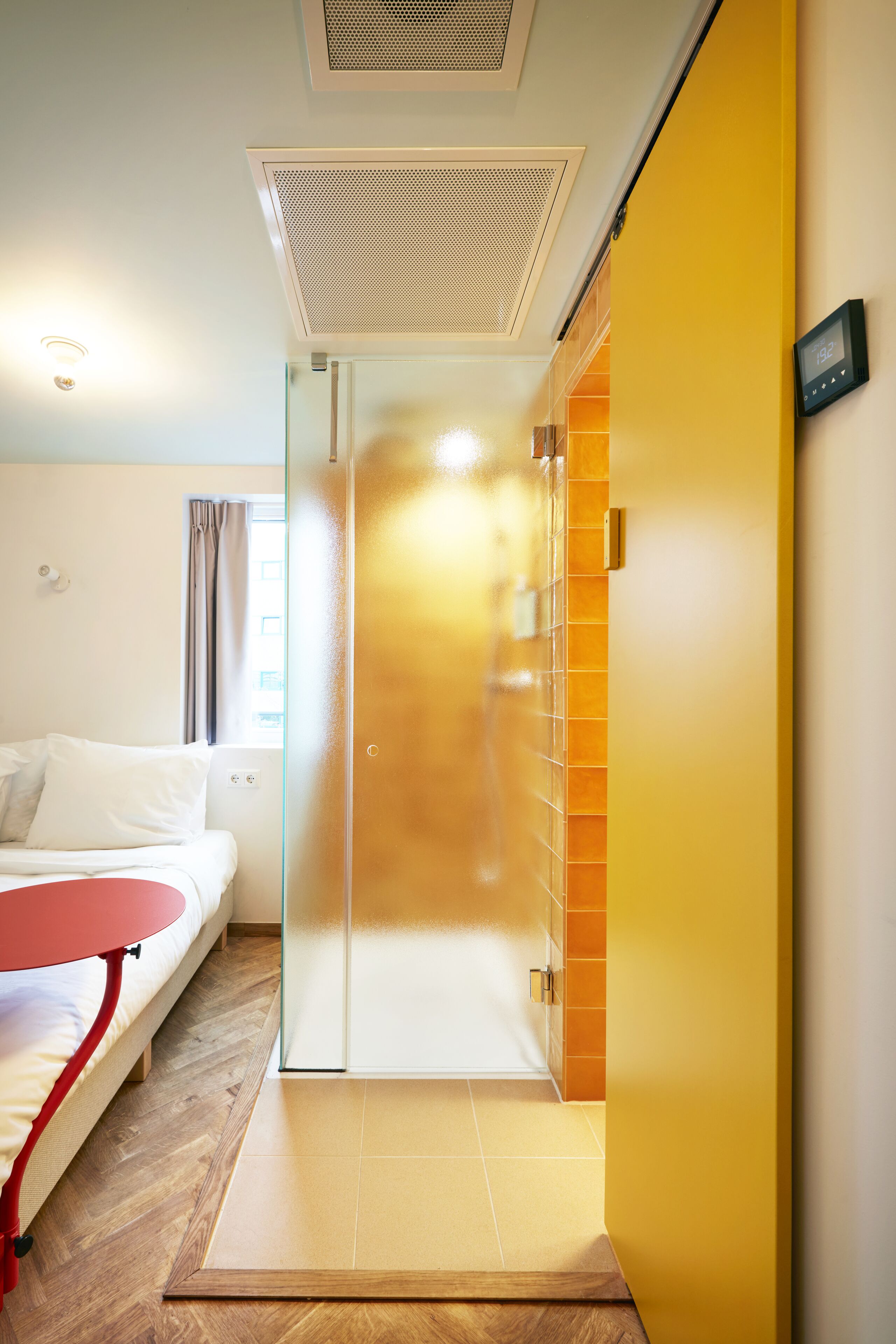 Una habitación de hotel con cama, una mesita pequeña, una puerta corredera y un termostato en la pared.