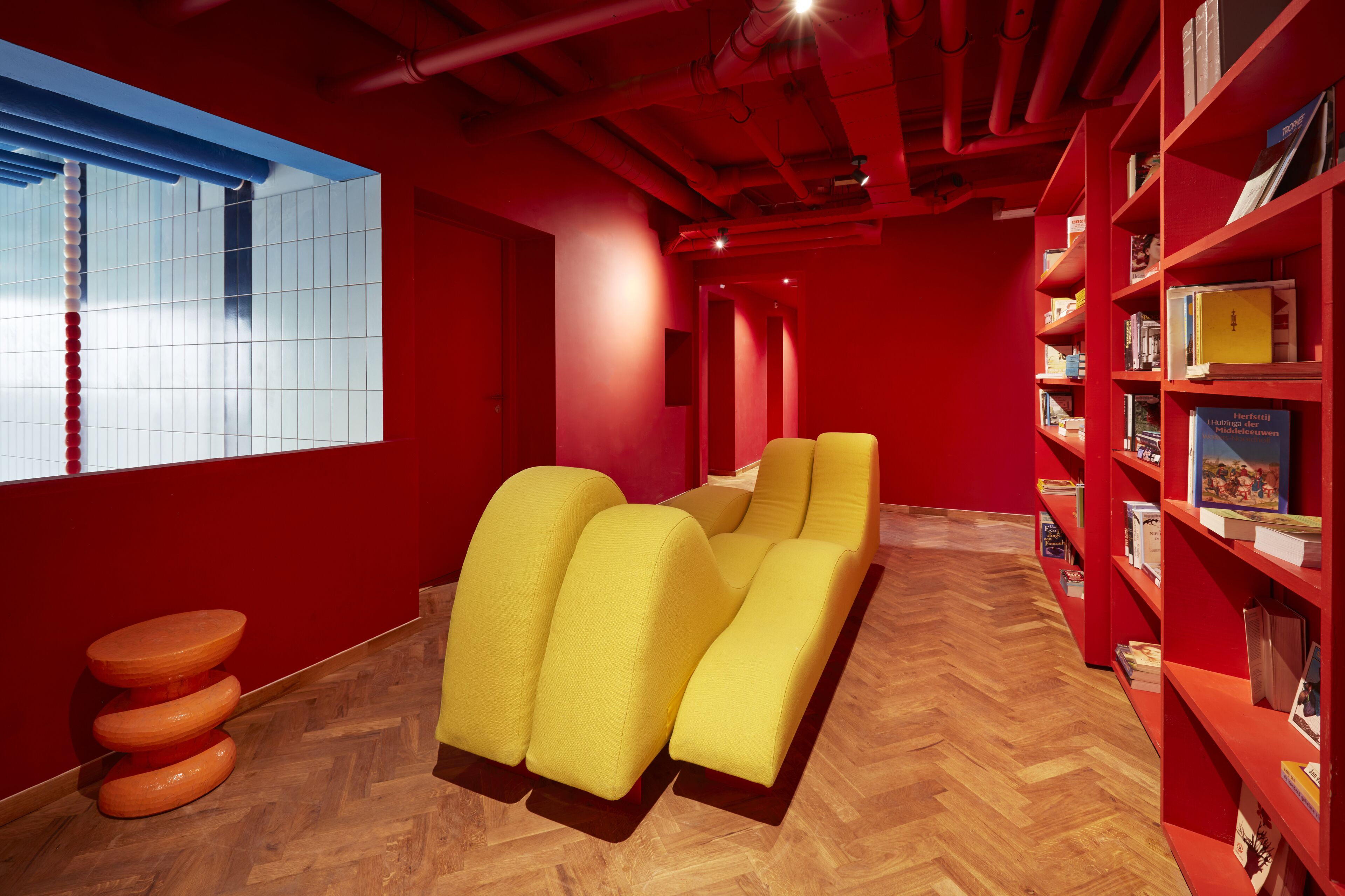 Una biblioteca moderna con paredes rojas, suelo de madera y zonas de estar con asientos amarillos.