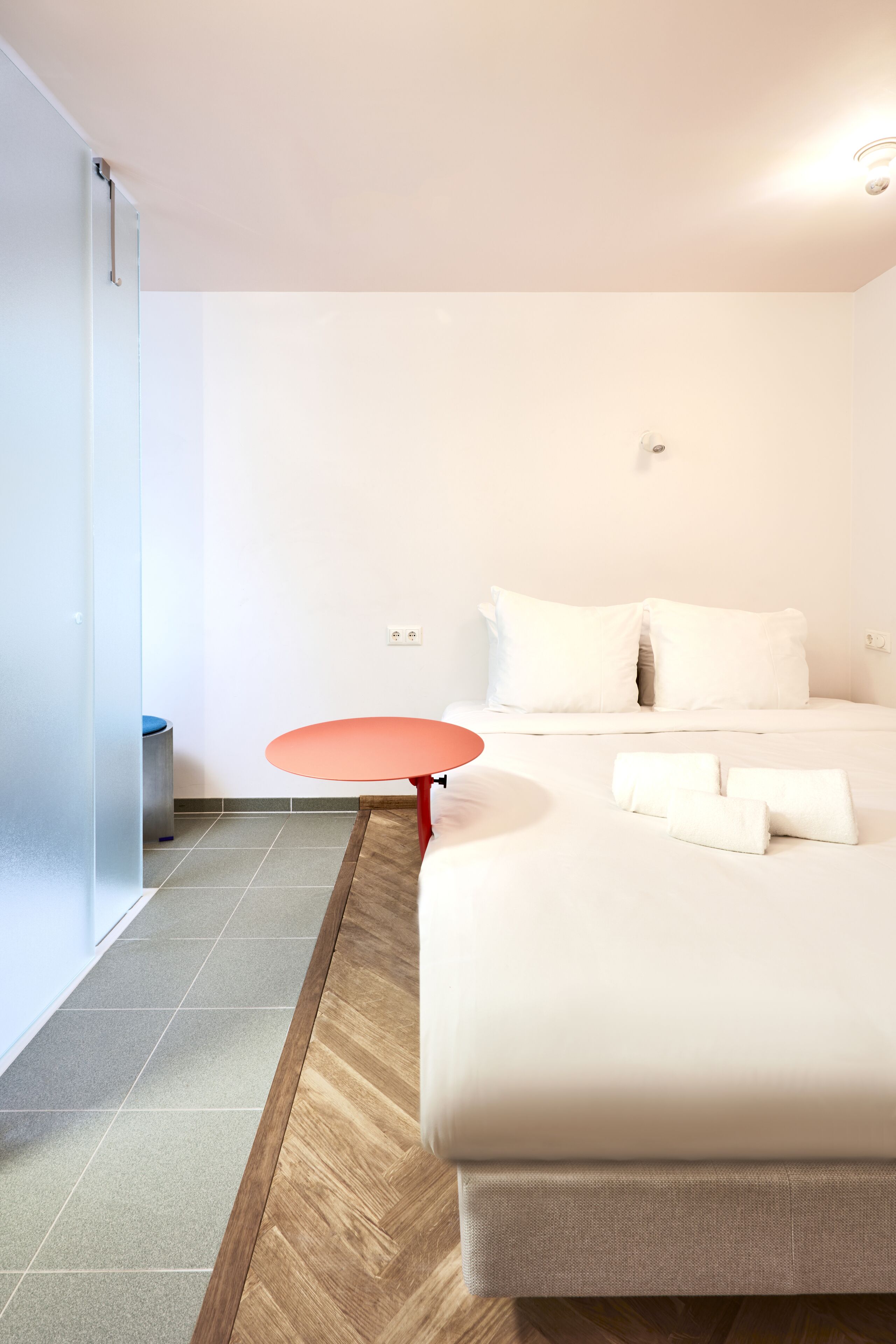 A modern hotel room with a large bed, a small round table, and a sliding door.