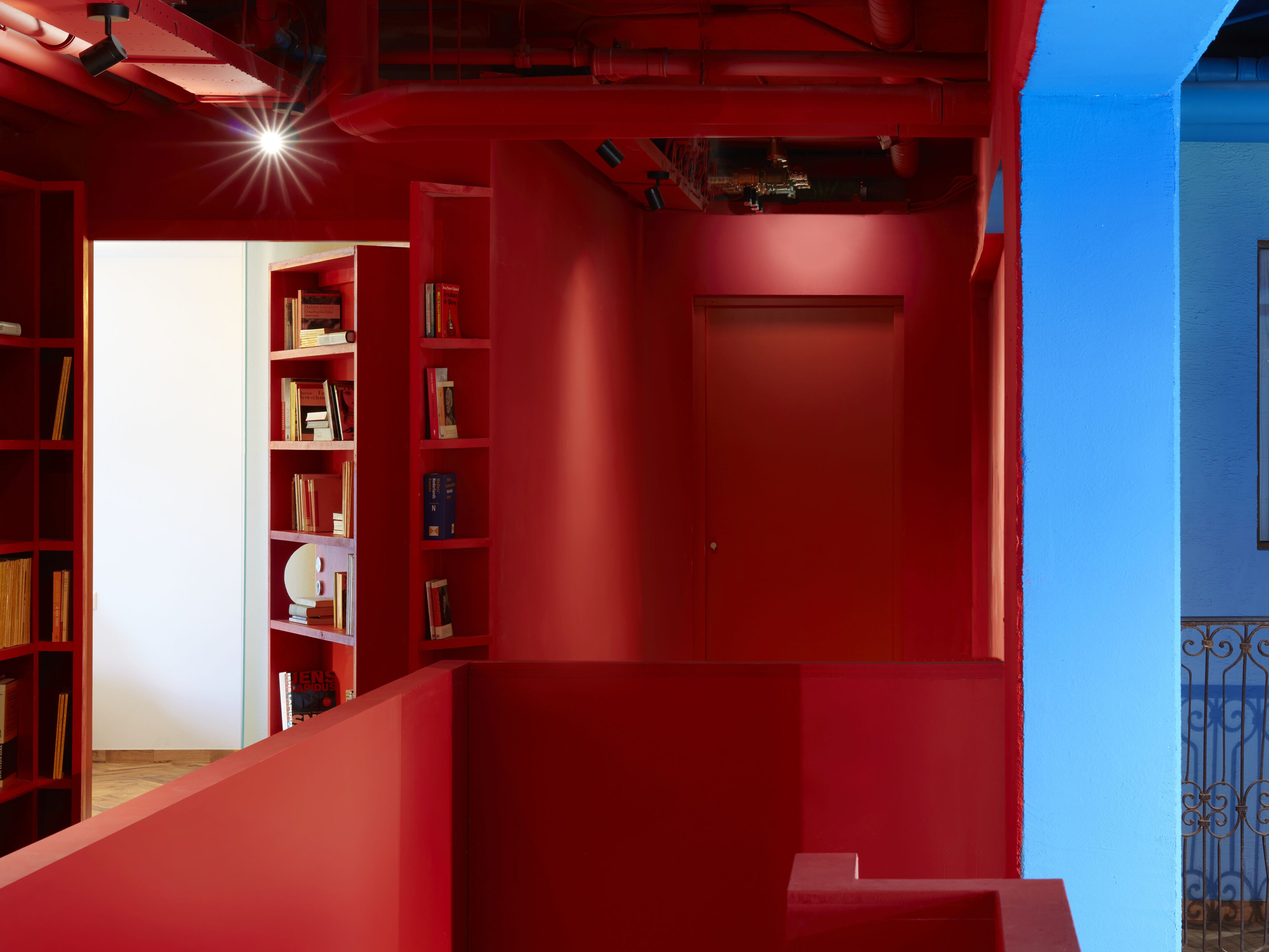 Un interno rosso con una libreria, una porta chiusa e un muro blu.