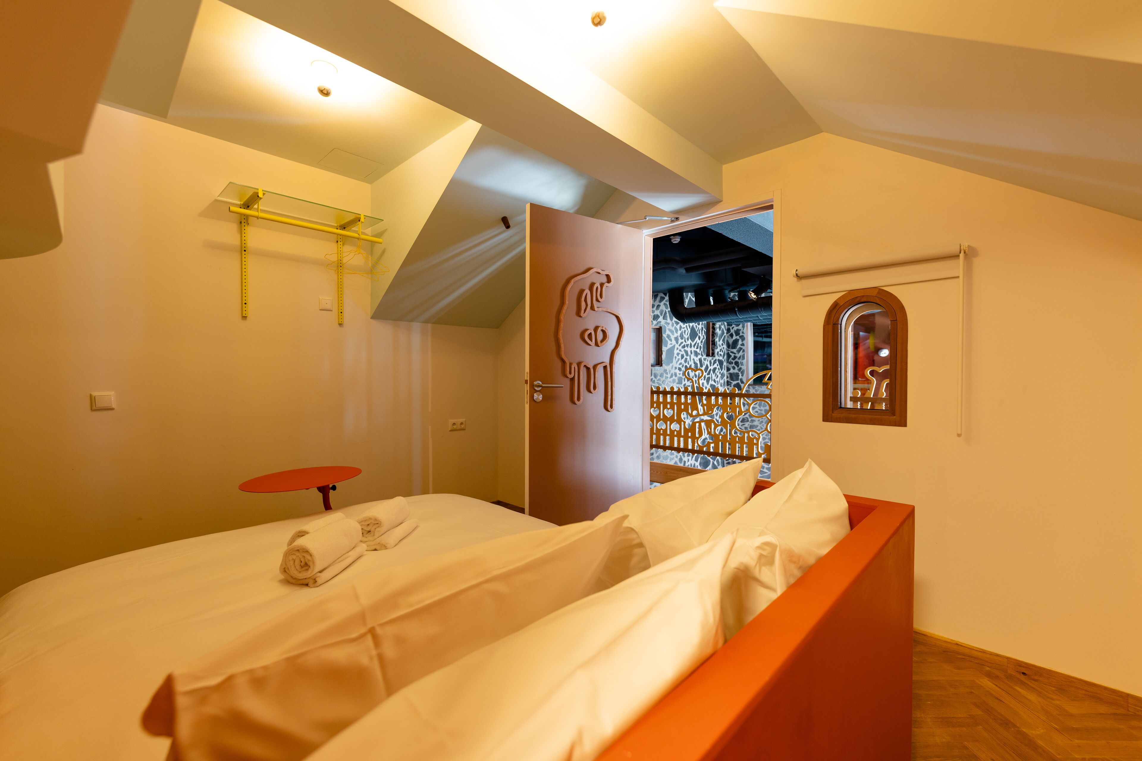 A hotel room with a bed, a red table, and a door leading to a bathroom.