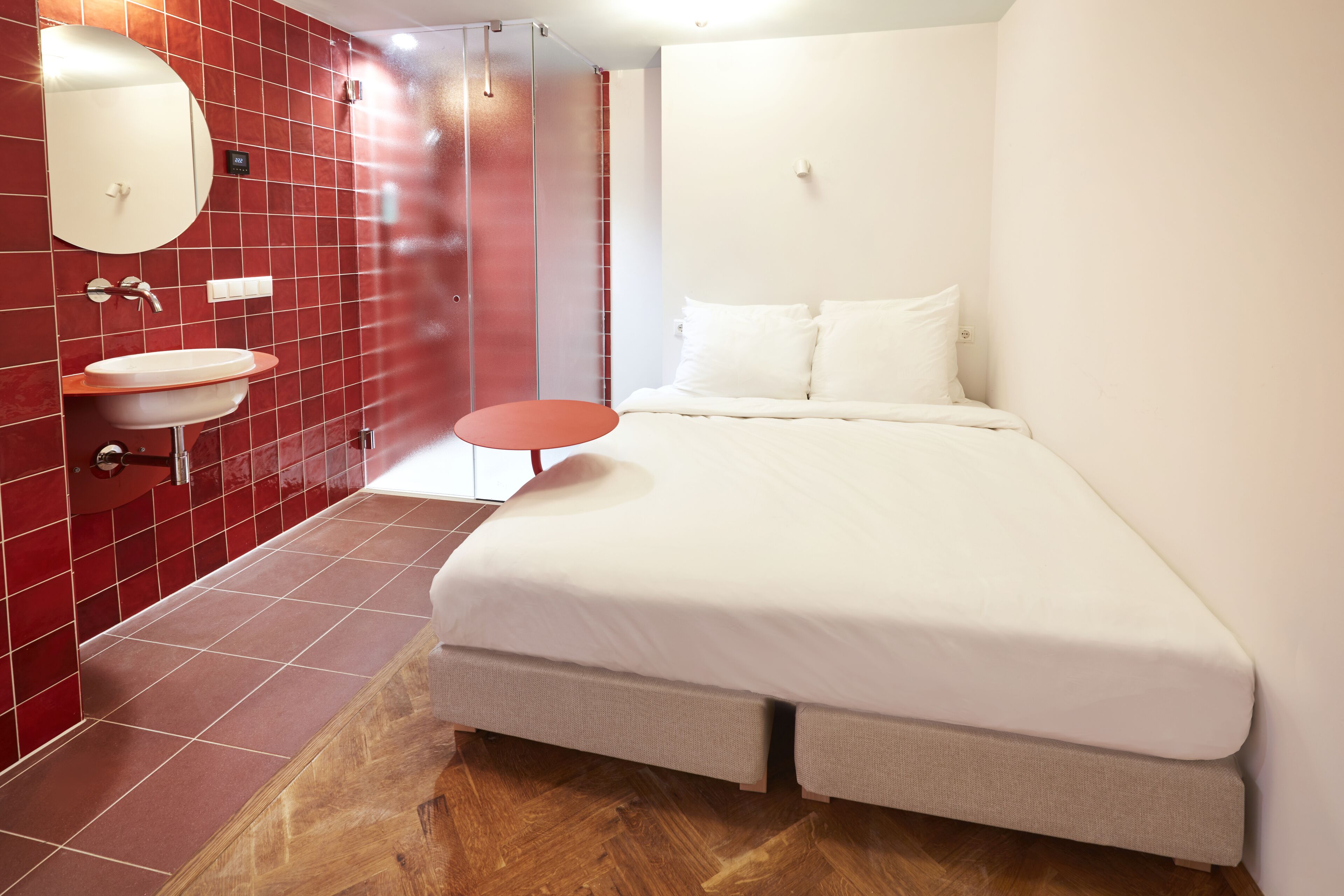 Moderni hotellihuone, jossa on suuri sänky, pieni pyöreä pöytä, pesuallas ja peili.