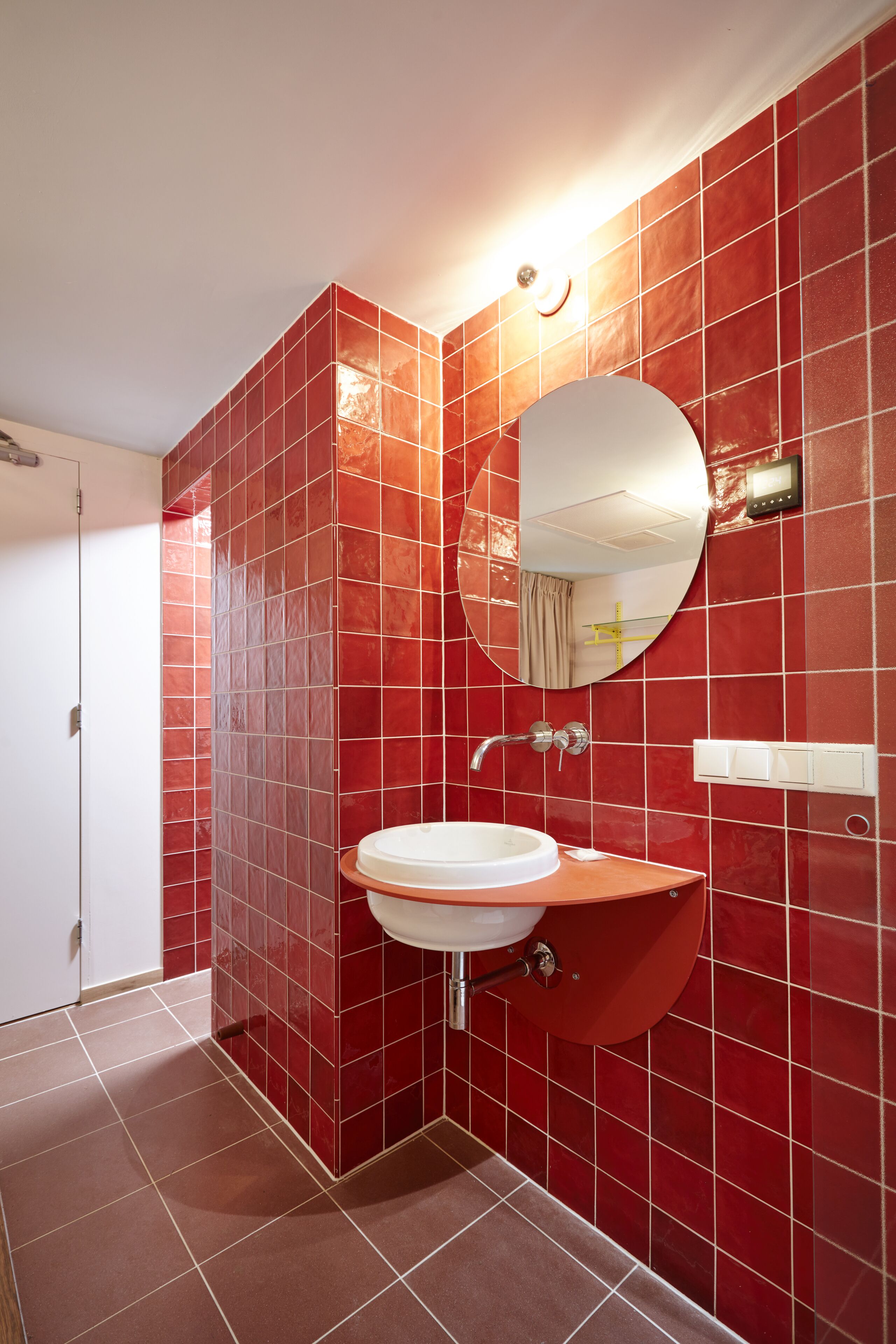 A bathroom with red tiled walls, a white sink, and a round mirror.