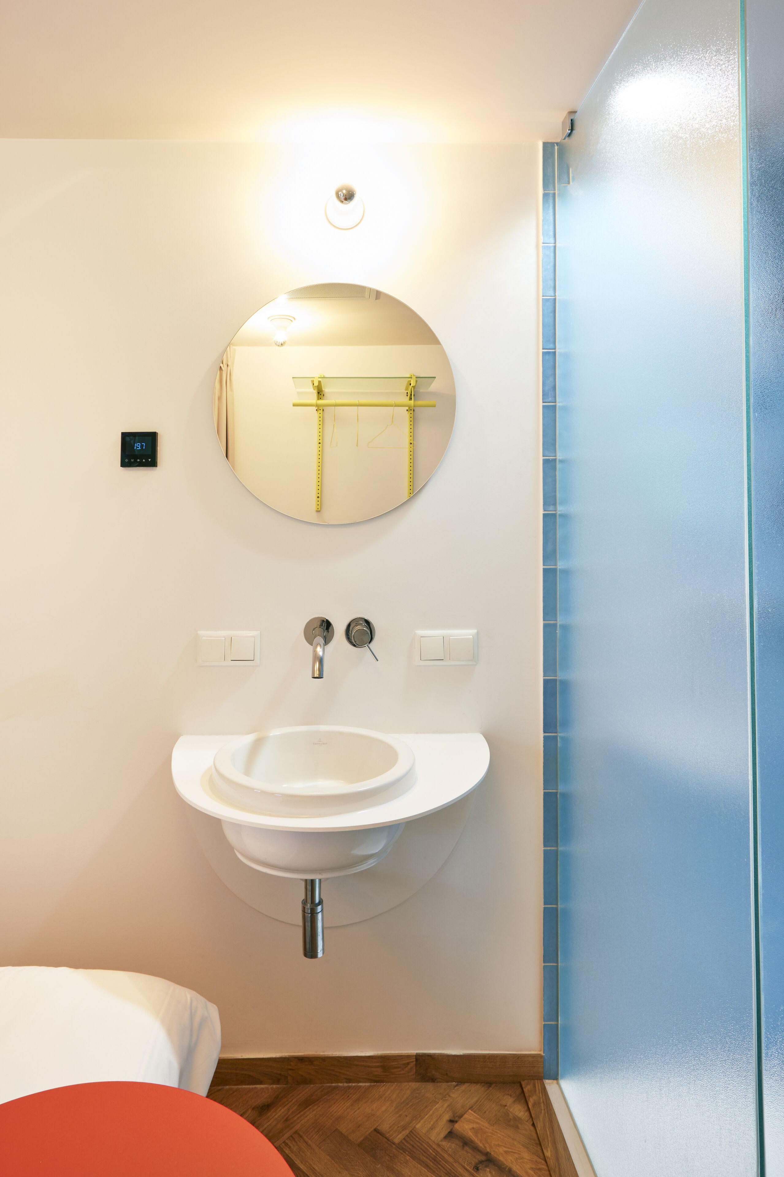 Un baño con un espejo redondo, un lavamanos blanco y un inodoro.