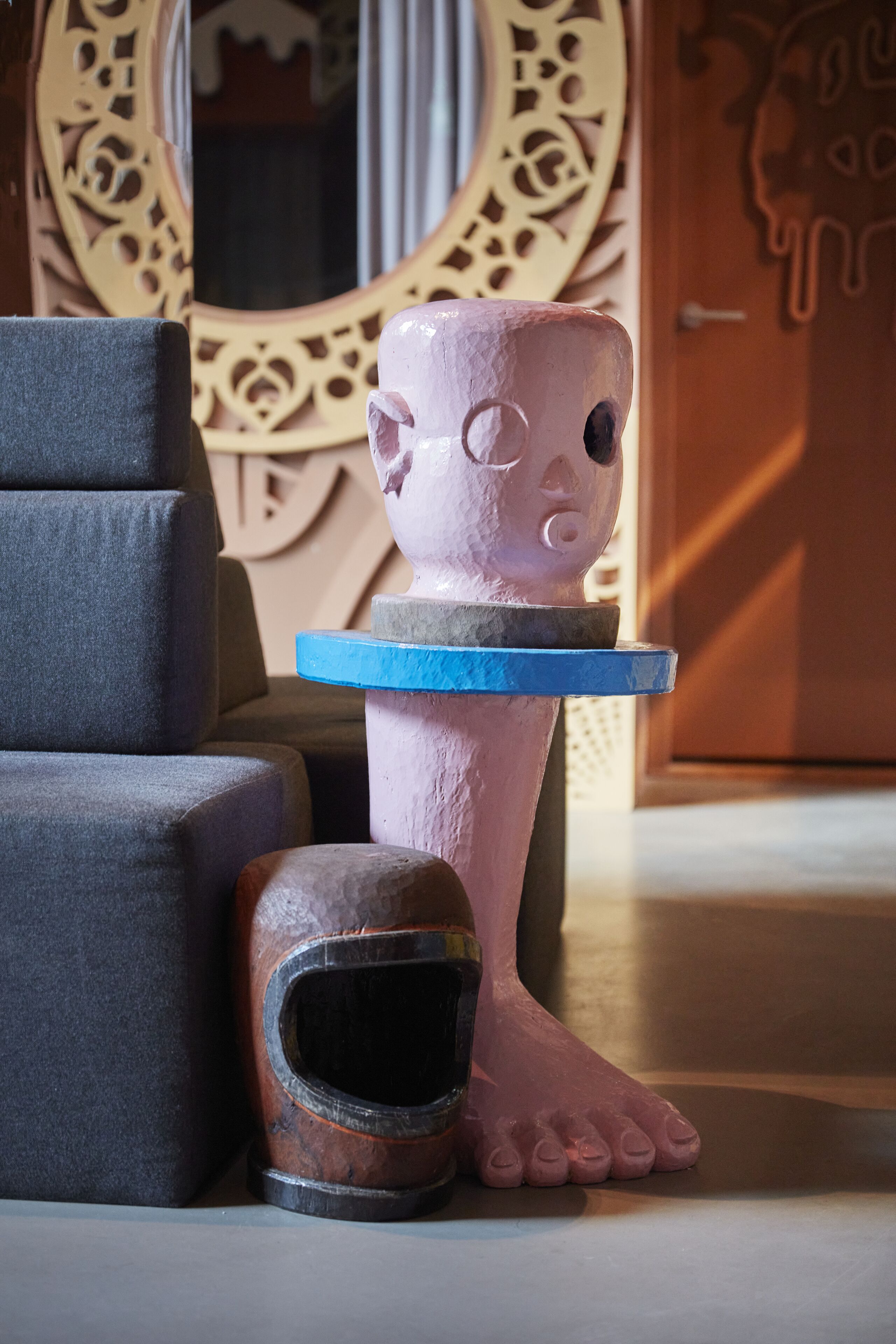 Een sculptuur toont een figuur bij een blauw platform, een stoel en een deur met decoratief ontwerp.