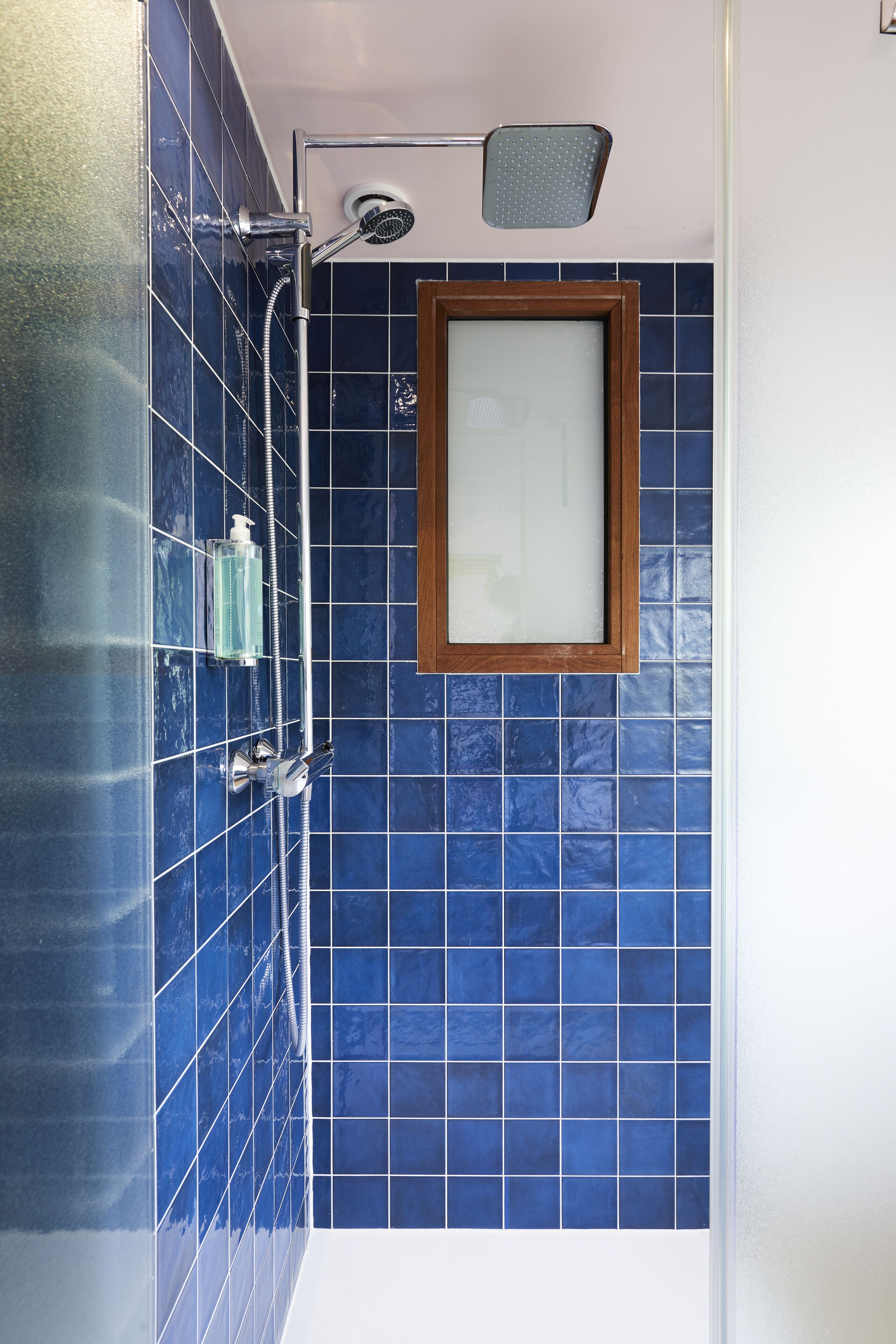 Un baño con azulejos azules, ducha y espejo con marco de madera.