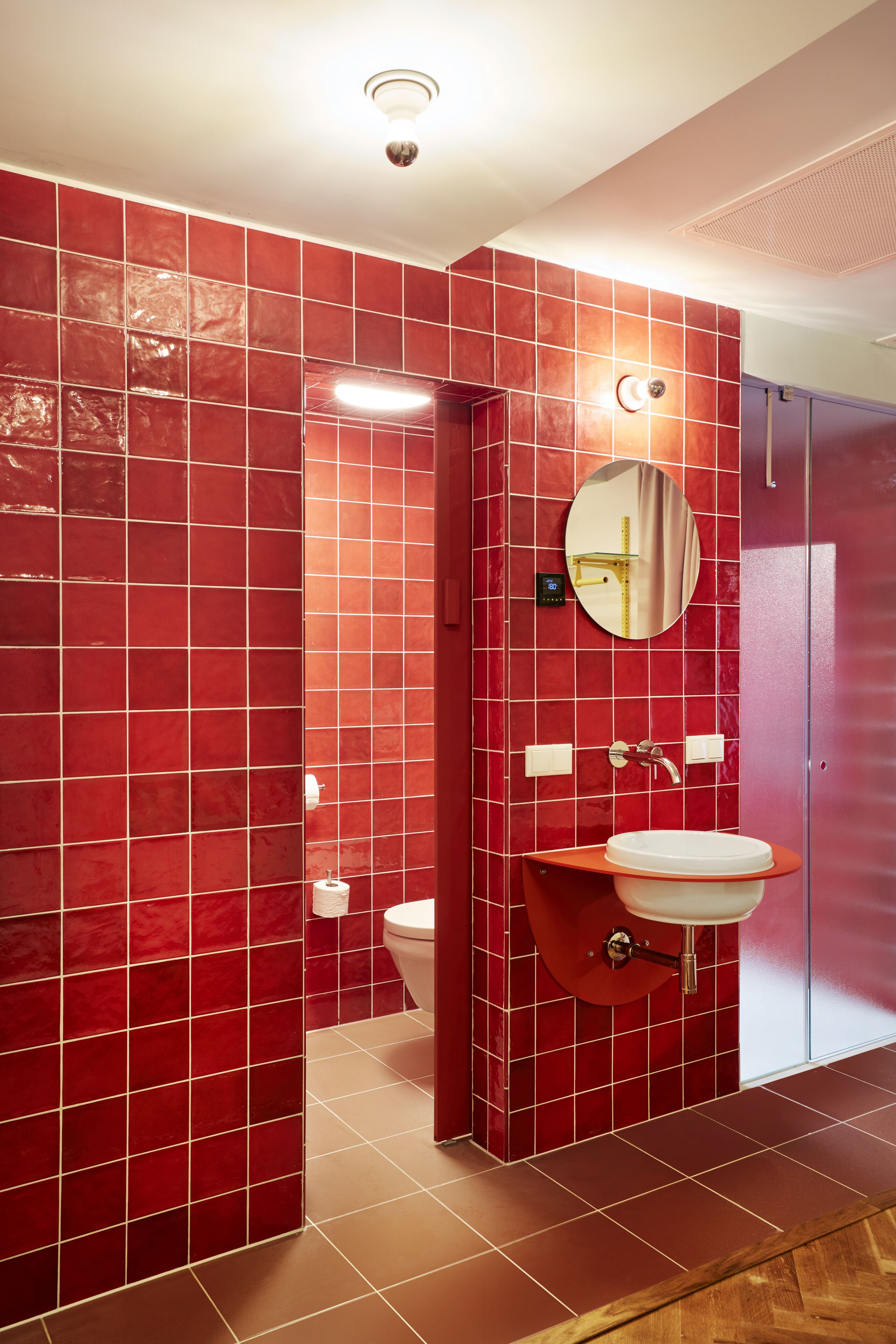 Un baño con paredes de azulejos rojos, un lavabo blanco y un espejo.