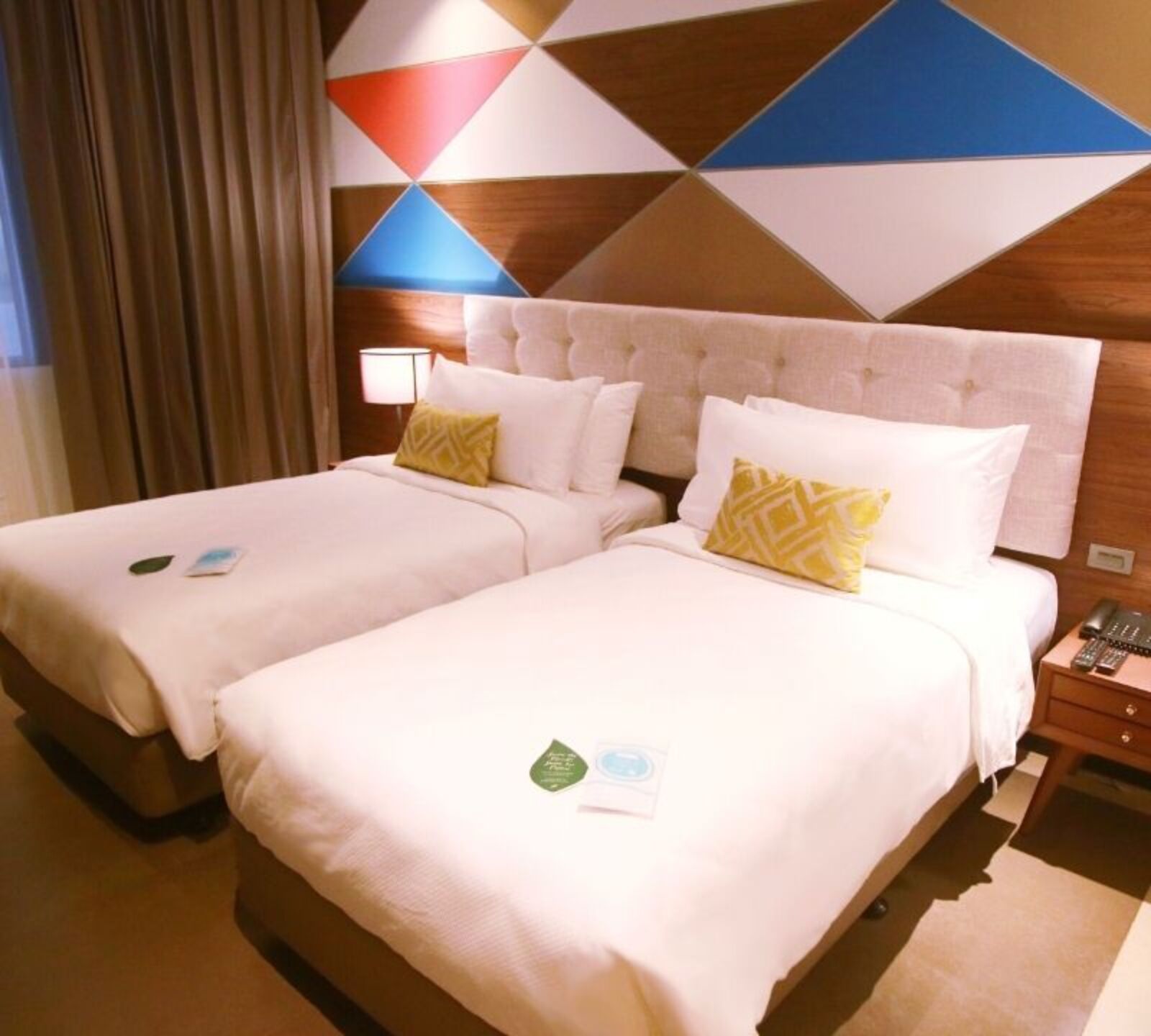 A hotel room with two beds, a wooden headboard, a nightstand with a phone, and a geometric-patterned wall.