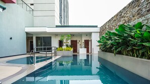 Una piscina de diseño moderno, rodeada por un edificio blanco y un muro de piedra.