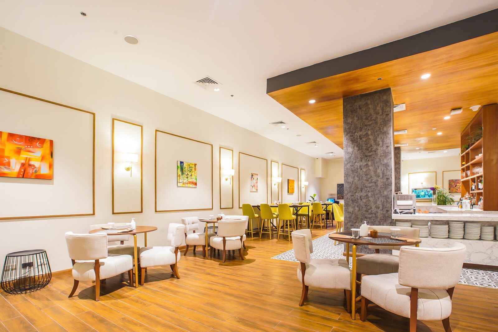 Un moderno vestíbulo de hotel con piso de madera, sillas blancas y amarillas, y obras de arte en las paredes.