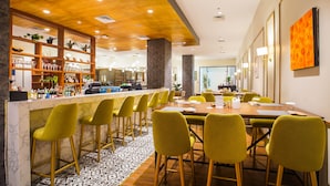 Un moderno vestíbulo de hotel con zona de bar, sillas amarillas y una gran mesa de comedor.