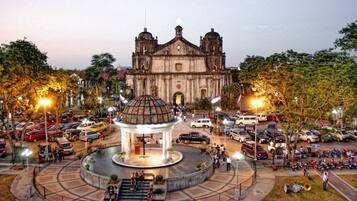 A historic building with a central dome and two bell towers, surrounded by a circular plaza with a fountain and seating areas.