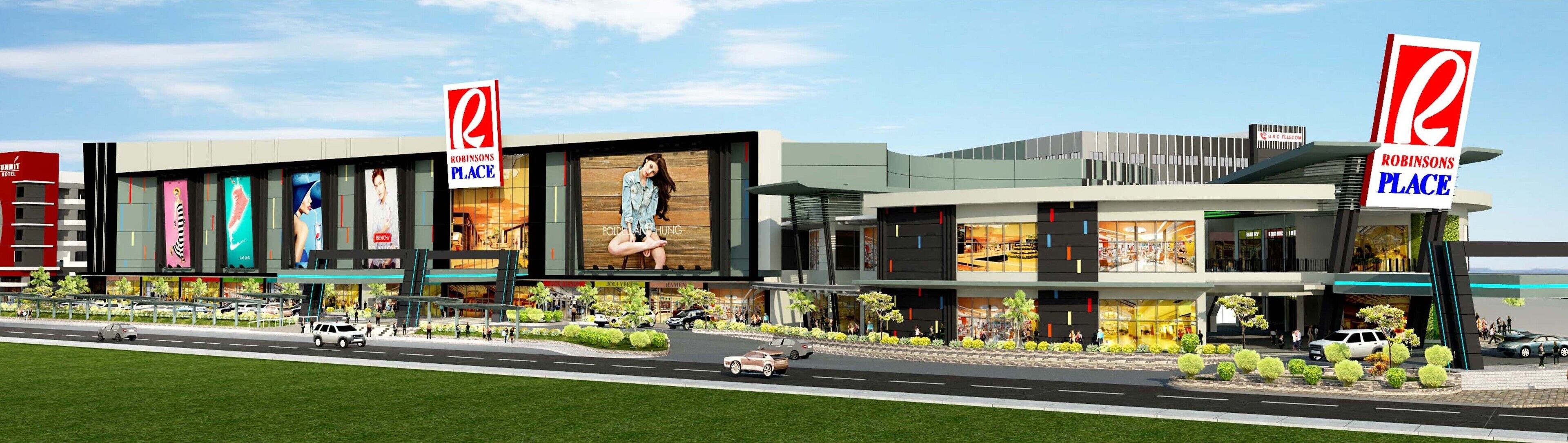 Un bâtiment moderne abritant plusieurs magasins Robinsons Place, un parking et une route où circulent des véhicules.