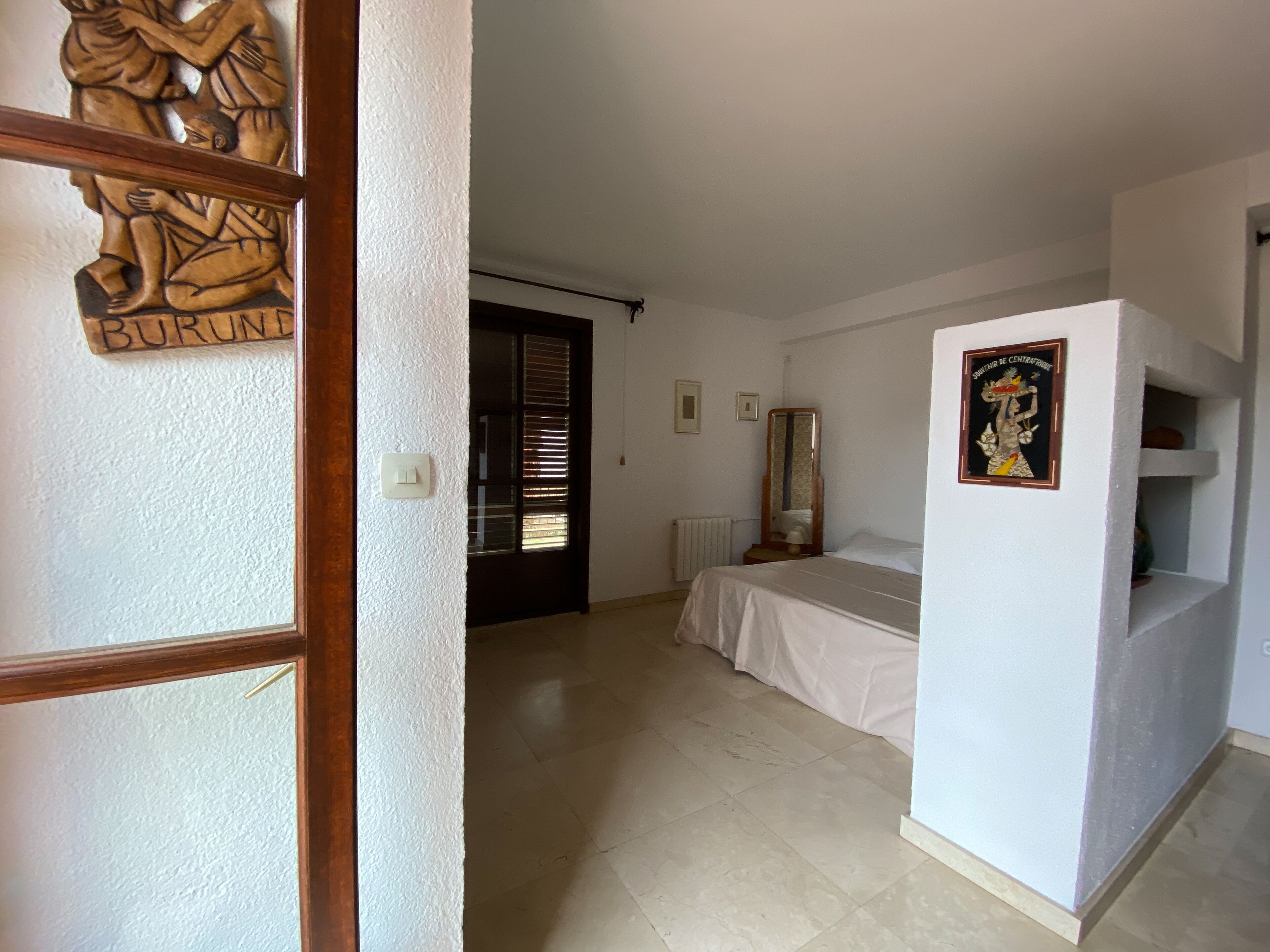 Un dormitorio con cama, cómoda, espejo y puerta con tallado de madera.