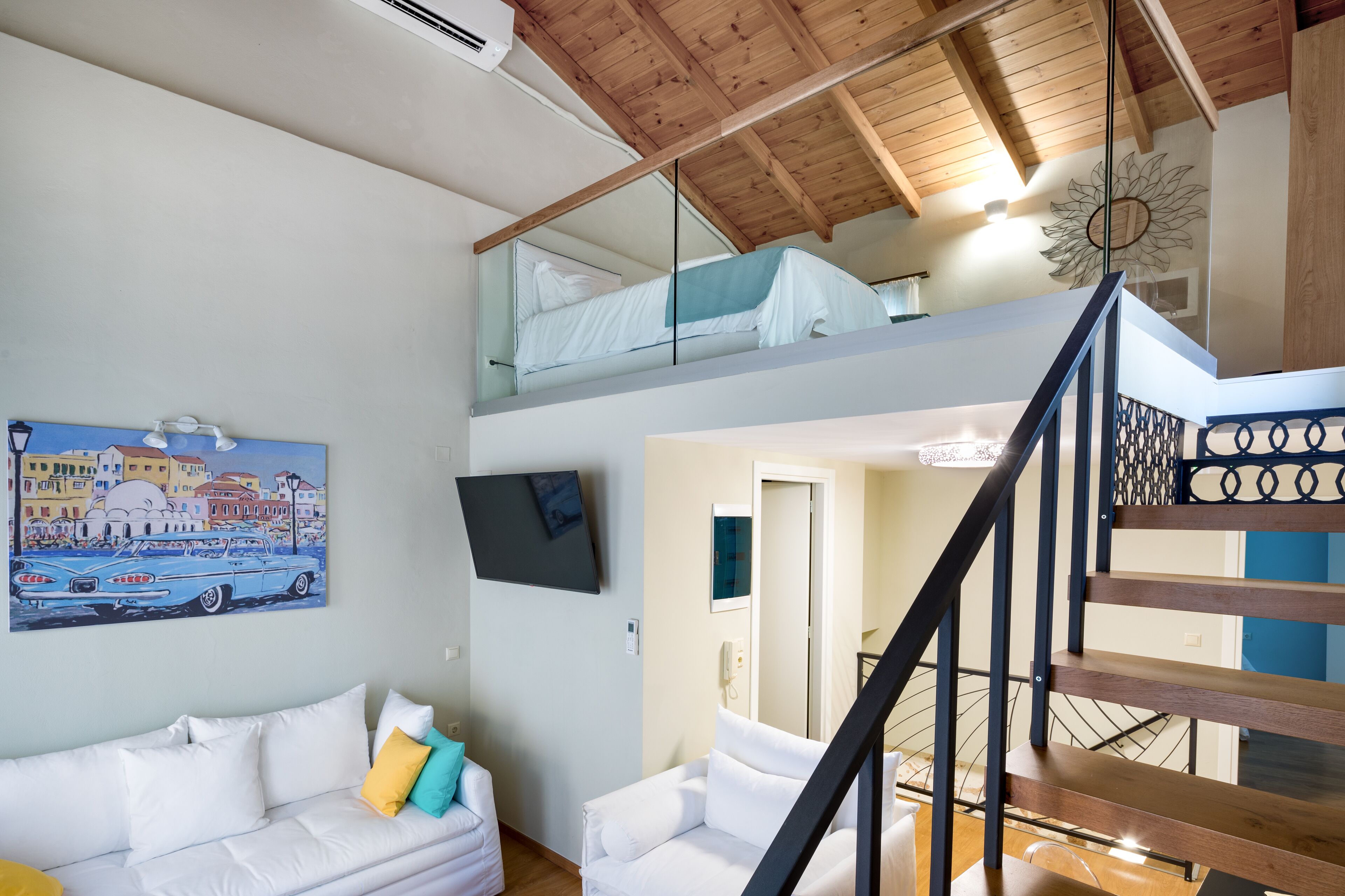 A modern interior with a white sofa, a painting of a car, and a staircase leading to a loft bedroom.