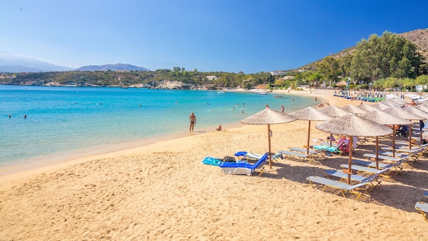 Ein Strand mit klarem türkisblauem Wasser, Liegestühlen und Sonnenschirmen.
