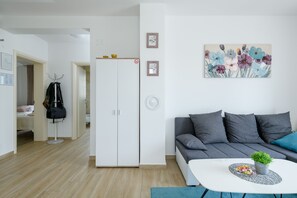 Un salon moderne avec un canapé gris, une table basse blanche ornée d’une plante et un tableau représentant des fleurs accroché au mur.