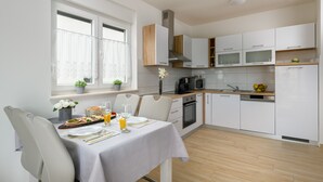 A modern kitchen with white cabinets, a microwave, and a sink. There's a dining table set with plates, glasses, and a fruit bowl. - Apartment Kate with balcony (Pula)
