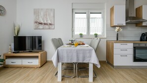 A modern kitchen with white cabinets, a built-in oven, and a dining area with a table set for two. - Apartment Kate with balcony (Pula)