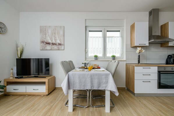 A modern kitchen with white cabinets, a built-in oven, and a dining area with a table set for two.