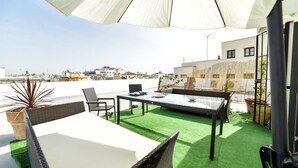 Eine Dachterrasse mit Tisch und Stühlen, einem großen Sonnenschirm und Blick auf die Stadt.