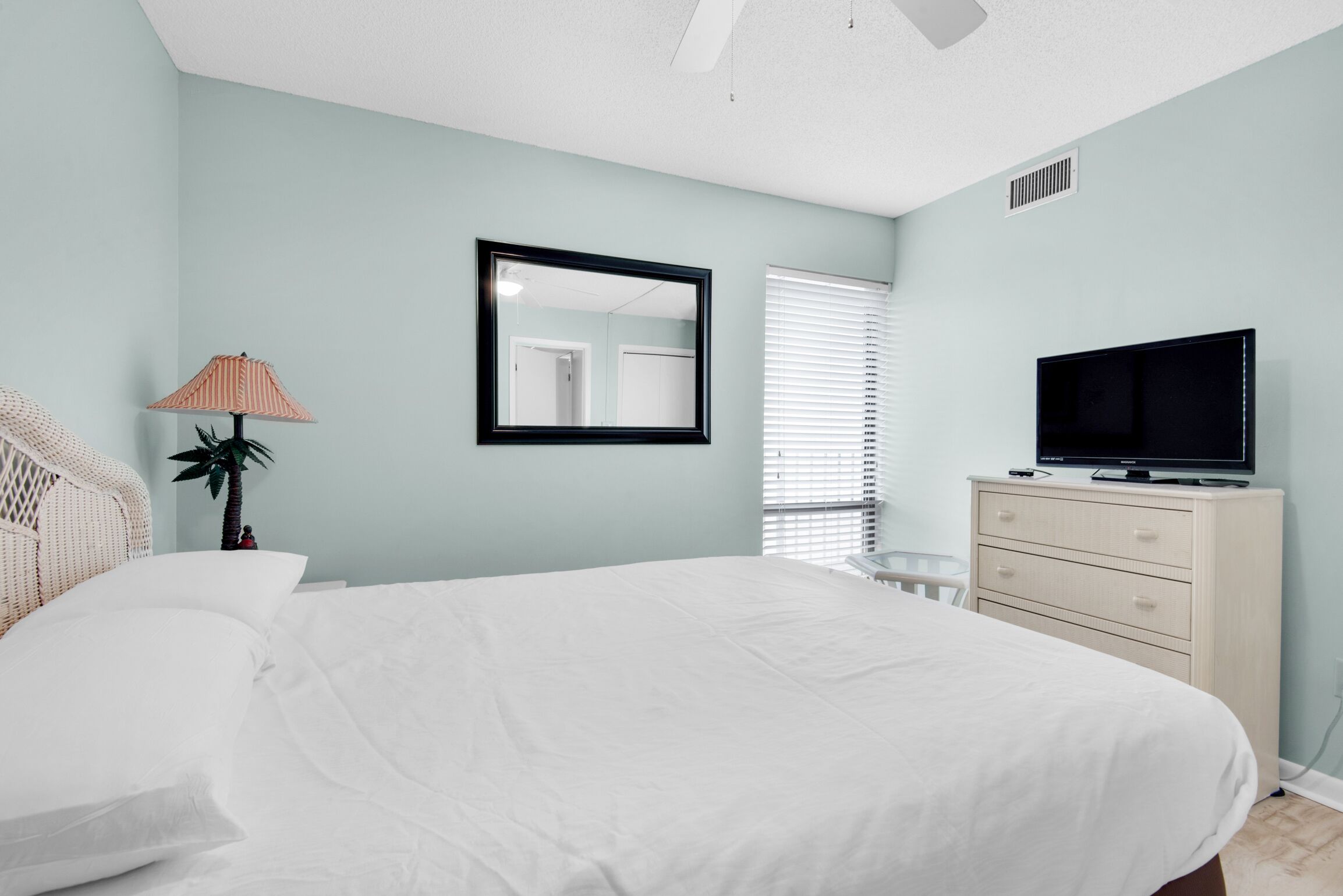 Un dormitorio con cama, cómoda, televisor, lámpara y ventana con persianas.