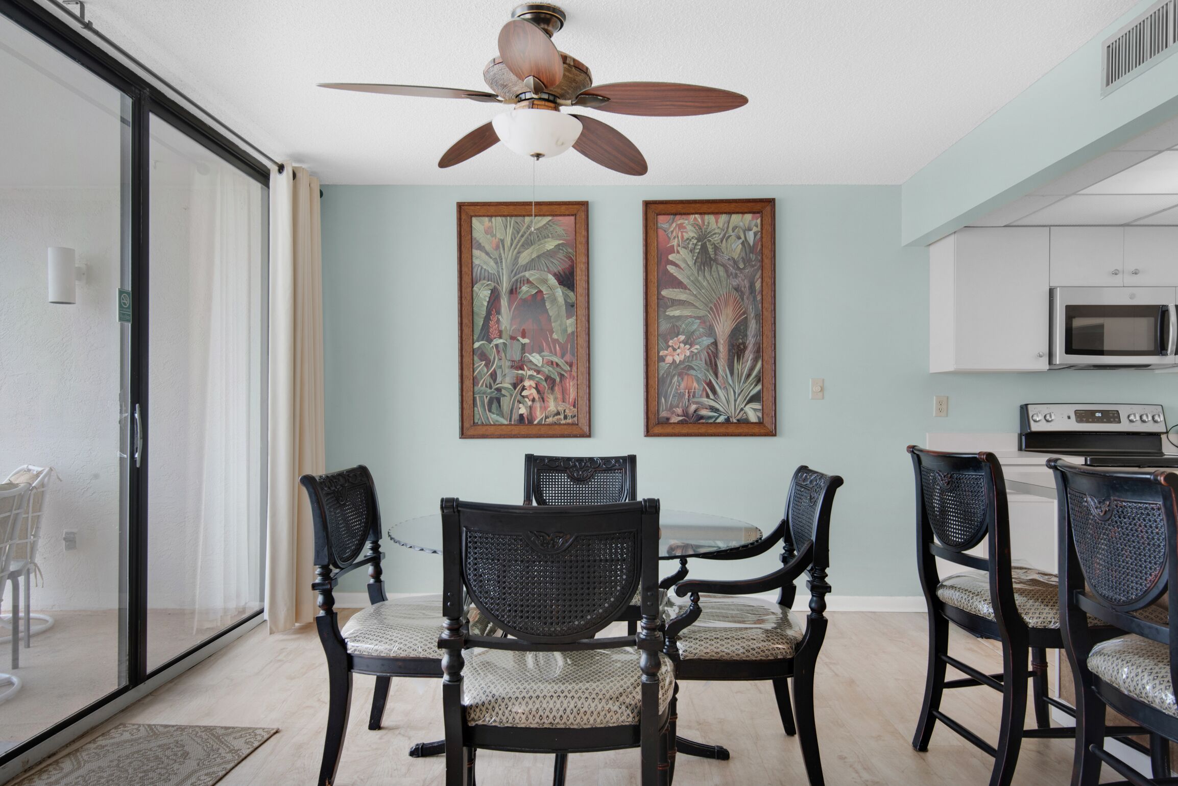Un comedor con una mesa redonda, seis sillas y dos cuadros enmarcados con motivos tropicales en la pared.
