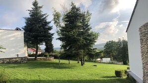 A well-maintained grassy yard with mature trees, stone walls, and a white building with a red roof. - Bultrak- eco village (Balchik)