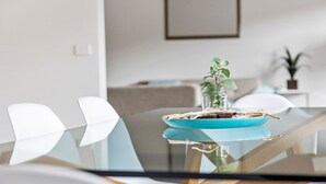 Un espace repas moderne avec une table en verre, des chaises blanches et une assiette bleue ornée d’une plante.