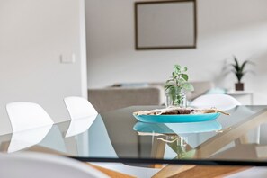 A modern dining area with a glass table, white chairs, and a blue plate with a plant. - Ocean Haven - In the heart of Fairhaven, Wi-Fi and Pet Friendly (Fairhaven)
