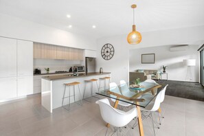 A modern kitchen with a central island, bar stools, a dining table with chairs, and a hanging pendant light. - Ocean Haven - In the heart of Fairhaven, Wi-Fi and Pet Friendly (Fairhaven)