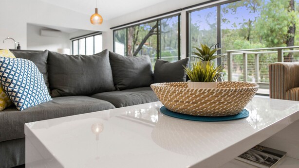 Un salon moderne avec un canapé gris, une table basse blanche et une grande fenêtre donnant sur un paysage verdoyant.