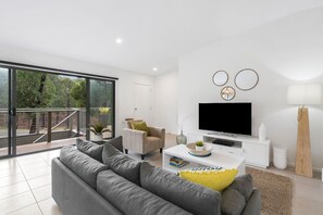 A modern living room with a grey sofa, a flat-screen TV, and a balcony with a view of trees. - Ocean Haven - In the heart of Fairhaven, Wi-Fi and Pet Friendly (Fairhaven)
