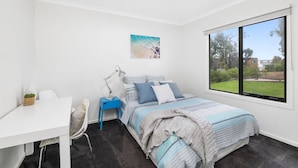 Une chambre à coucher avec un lit, un bureau, une chaise, une fenêtre et un tableau accroché au mur.