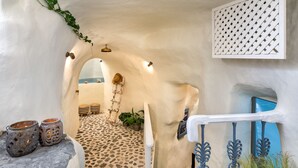 Un stretto passaggio con pavimento in pietra che conduce a vista mare, una scala e una porta con cornice blu.