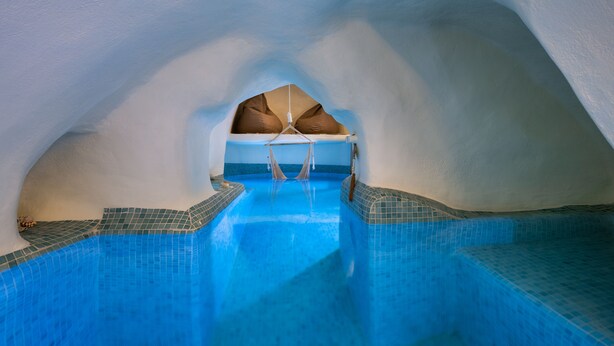 Interno di un hotel di ghiaccio con piscina centrale, balaustre in vetro trasparente e una poltrona sospesa.