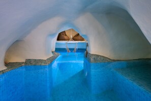 Interno di un hotel di ghiaccio con piscina centrale, balaustre in vetro trasparente e una poltrona sospesa.