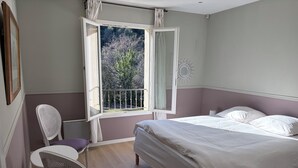 A bedroom with a bed, a chair, a window with curtains, and a view of trees outside. - Villa 170 m2 au Calme Avec Piscine 9,60 x 4,60 sur Terrain Paysagé de 3000m2 (Vence)