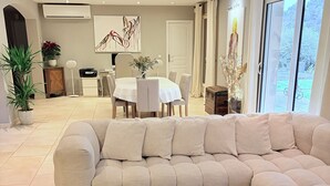 A living room with a sectional sofa, a wooden coffee table, and a dining area in the background. - Villa 170 m2 au Calme Avec Piscine 9,60 x 4,60 sur Terrain Paysagé de 3000m2 (Vence)