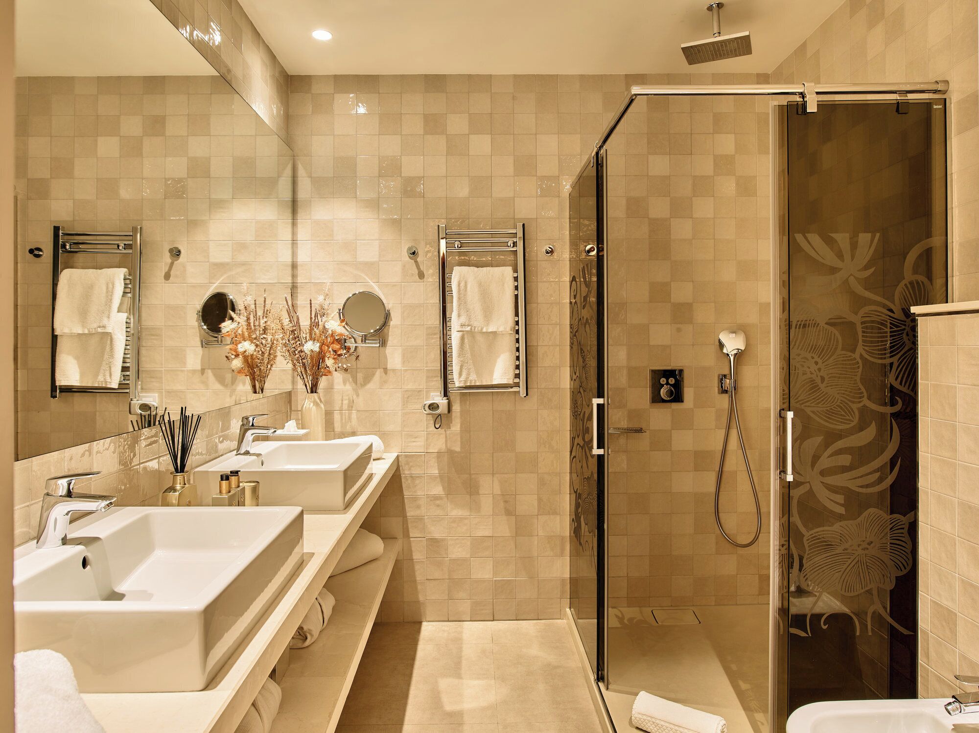 A modern bathroom with two sinks, a glass shower enclosure, and decorative wall tiles.