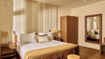 Habitación de hotel con una cama grande, un armario, un espejo y una mesita de noche con lámpara.