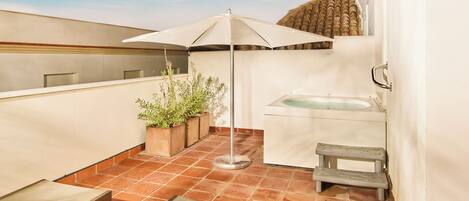 A rooftop terrace with a jacuzzi, a sun umbrella, potted plants, and a bench.