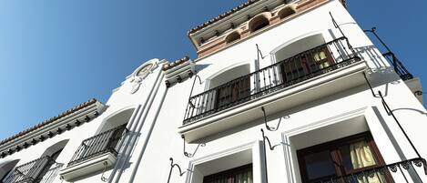 A multi-story building with white facades, multiple balconies with wrought iron railings, and a clear blue sky in the background.