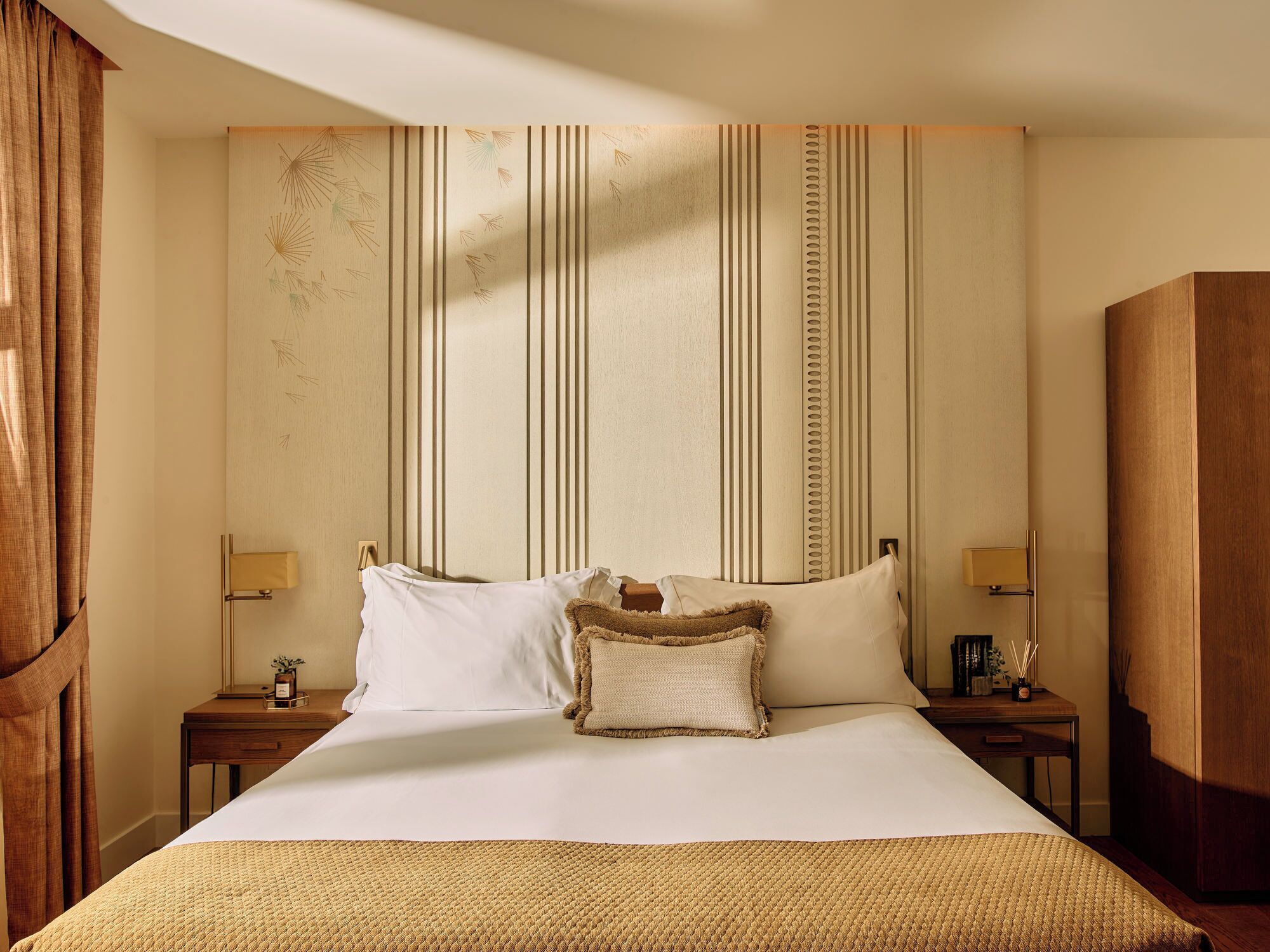 Una habitación de hotel con una cama grande, dos mesitas de noche, un armario de madera y un cabecero a rayas.