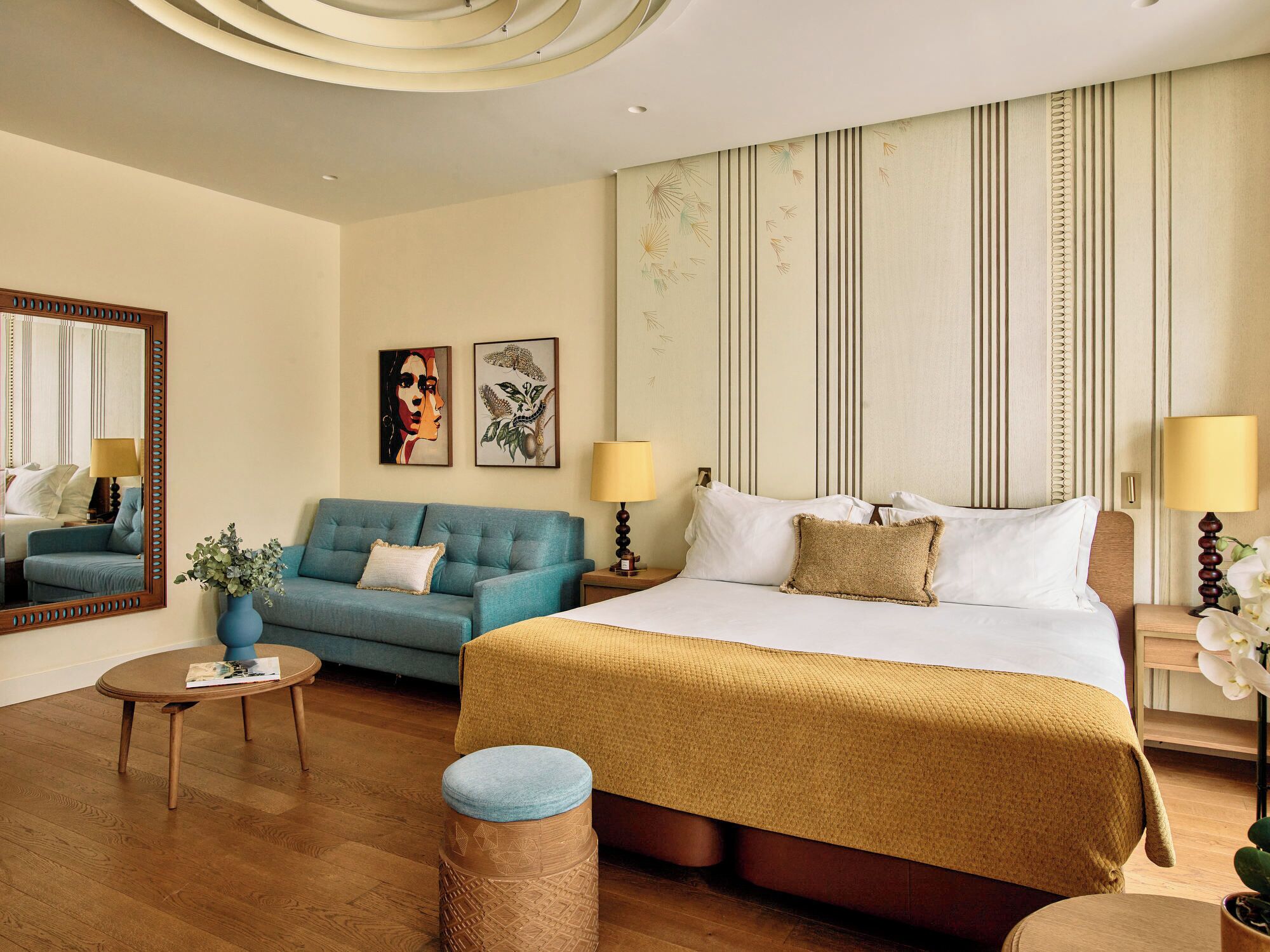 Una habitación de hotel con una cama grande, un sofá azul, una pequeña mesa redonda y un espejo.