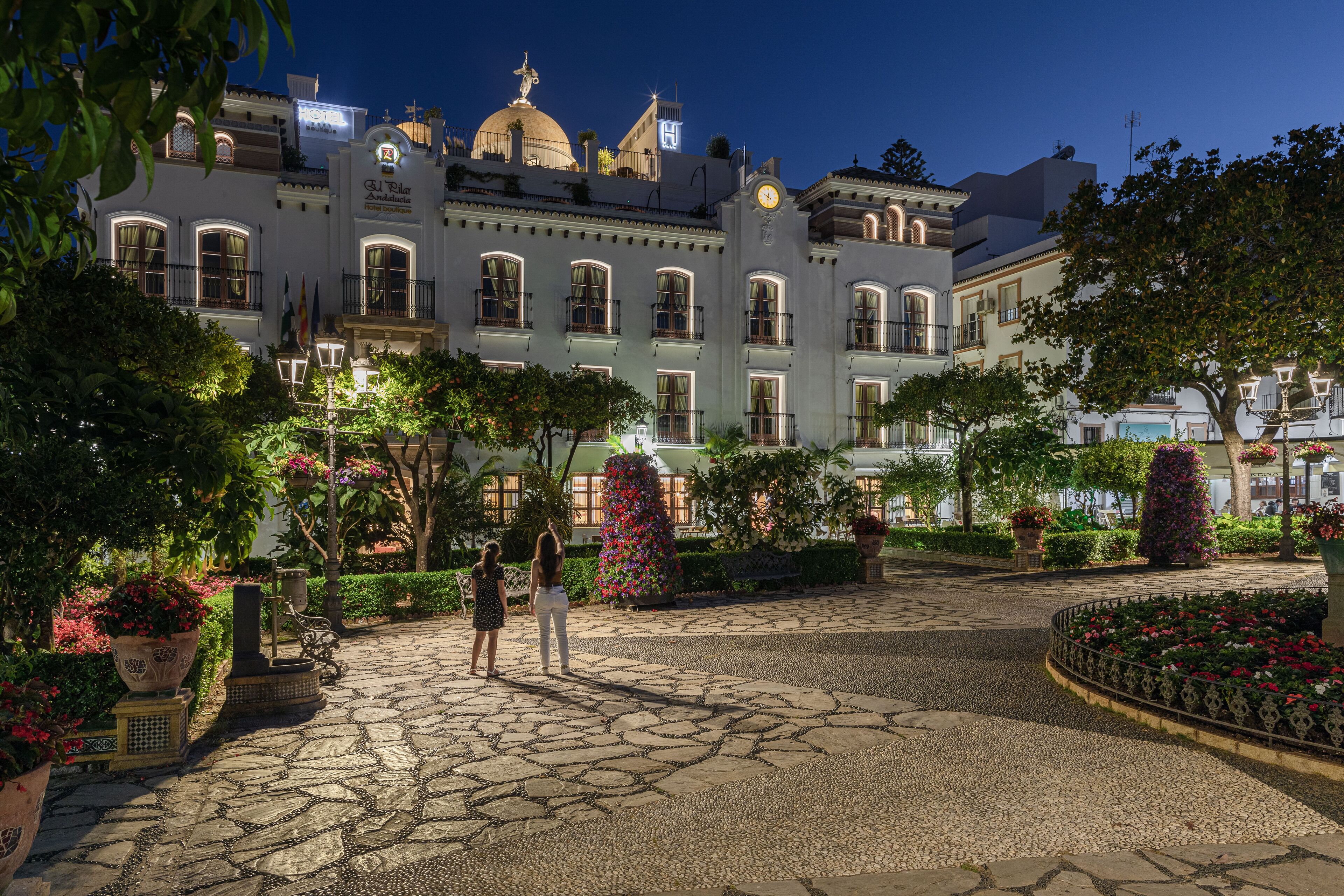 Un edificio histórico con cúpula y arquitectura clásica, rodeado de un jardín cuidado con senderos de piedra y plantas en macetas.