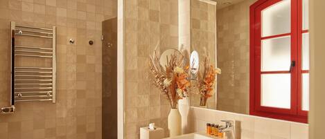 A modern bathroom with a beige tiled wall, a white sink, a mirror, and a red-framed window.